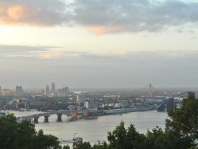Vista panorâmica de uma cidade atravessada por um rio largo, com pontes e prédios ao fundo sob céu nublado.